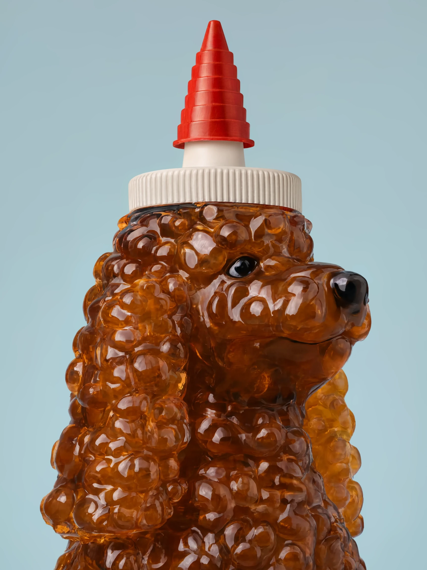 A honey bottle in the shape of a curly-coated poodle, filled with amber honey and capped with a red nozzle, against pale blue