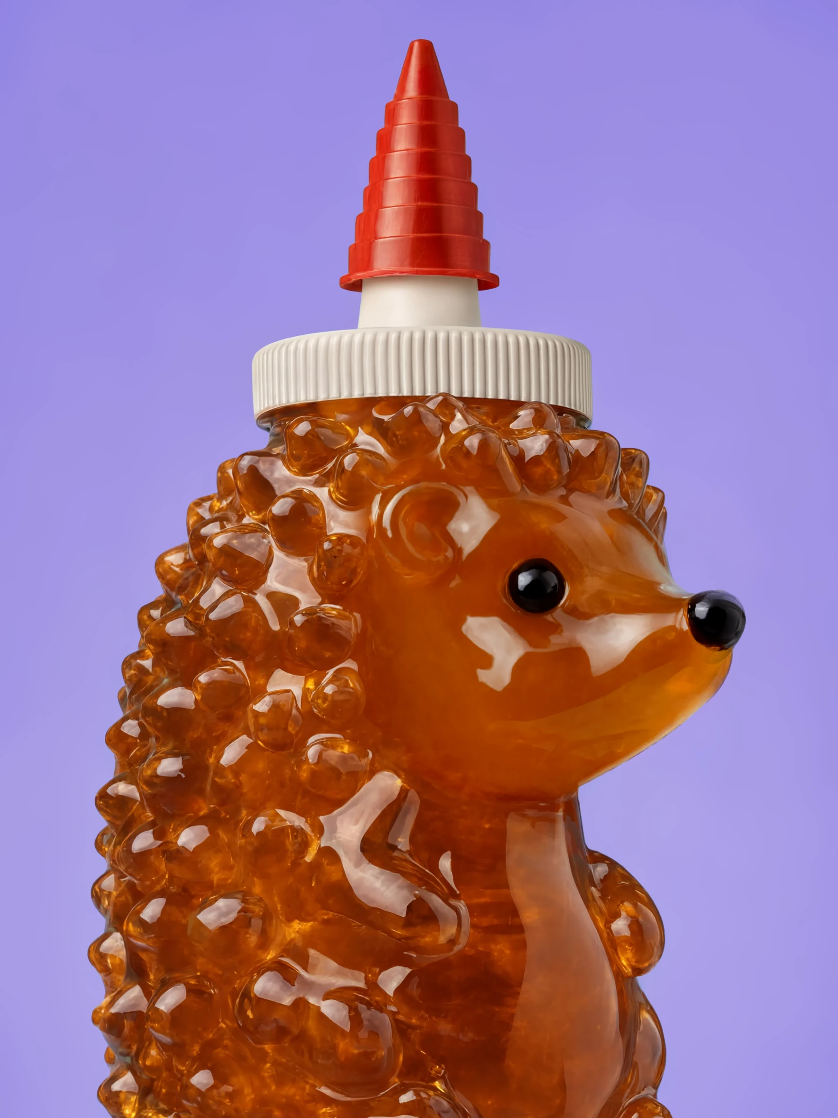 A honey bottle in the shape of a hedgehog, its spines rendered in amber glass and capped with a red nozzle, against lilac
