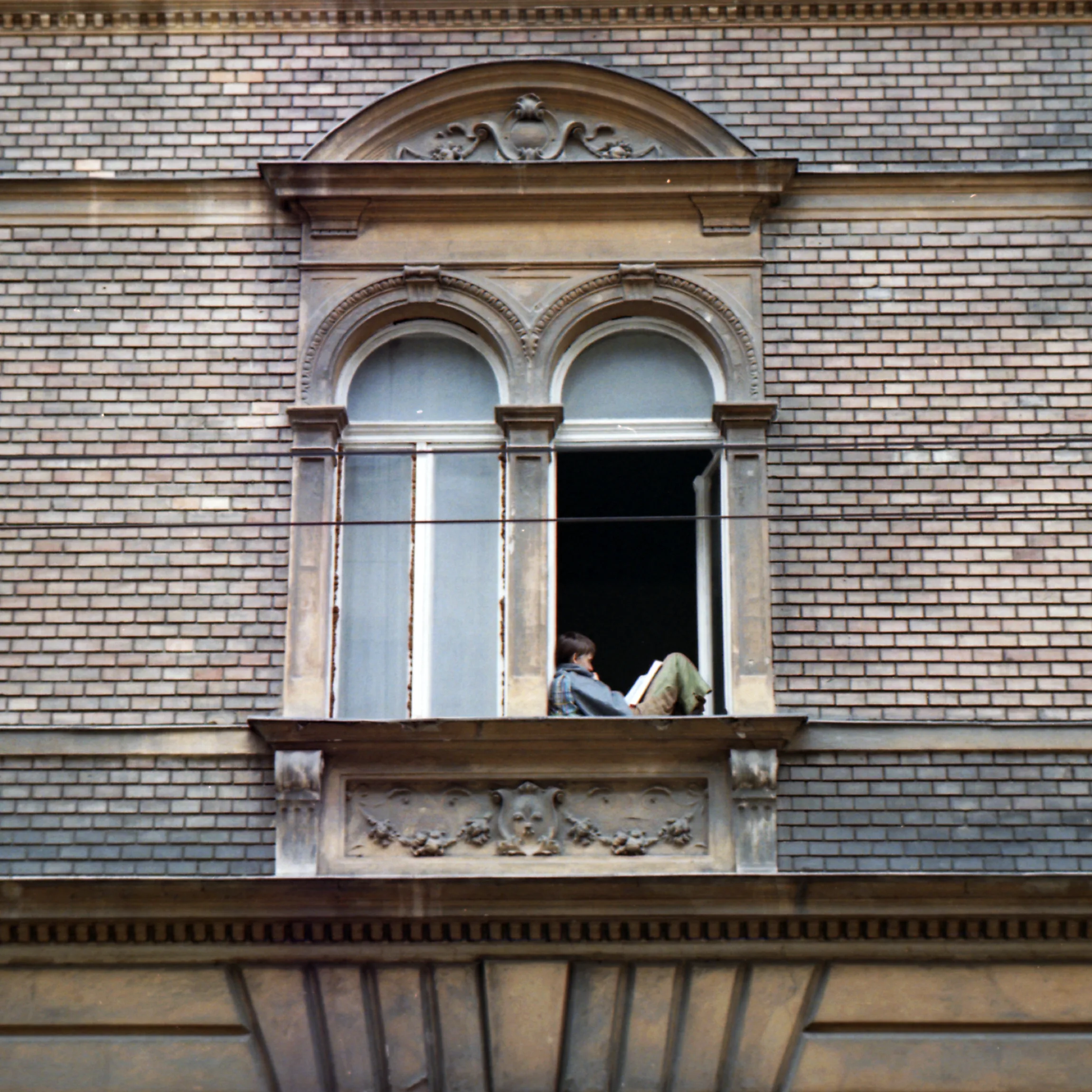 A person reading in the open window of an ornate brick facade
