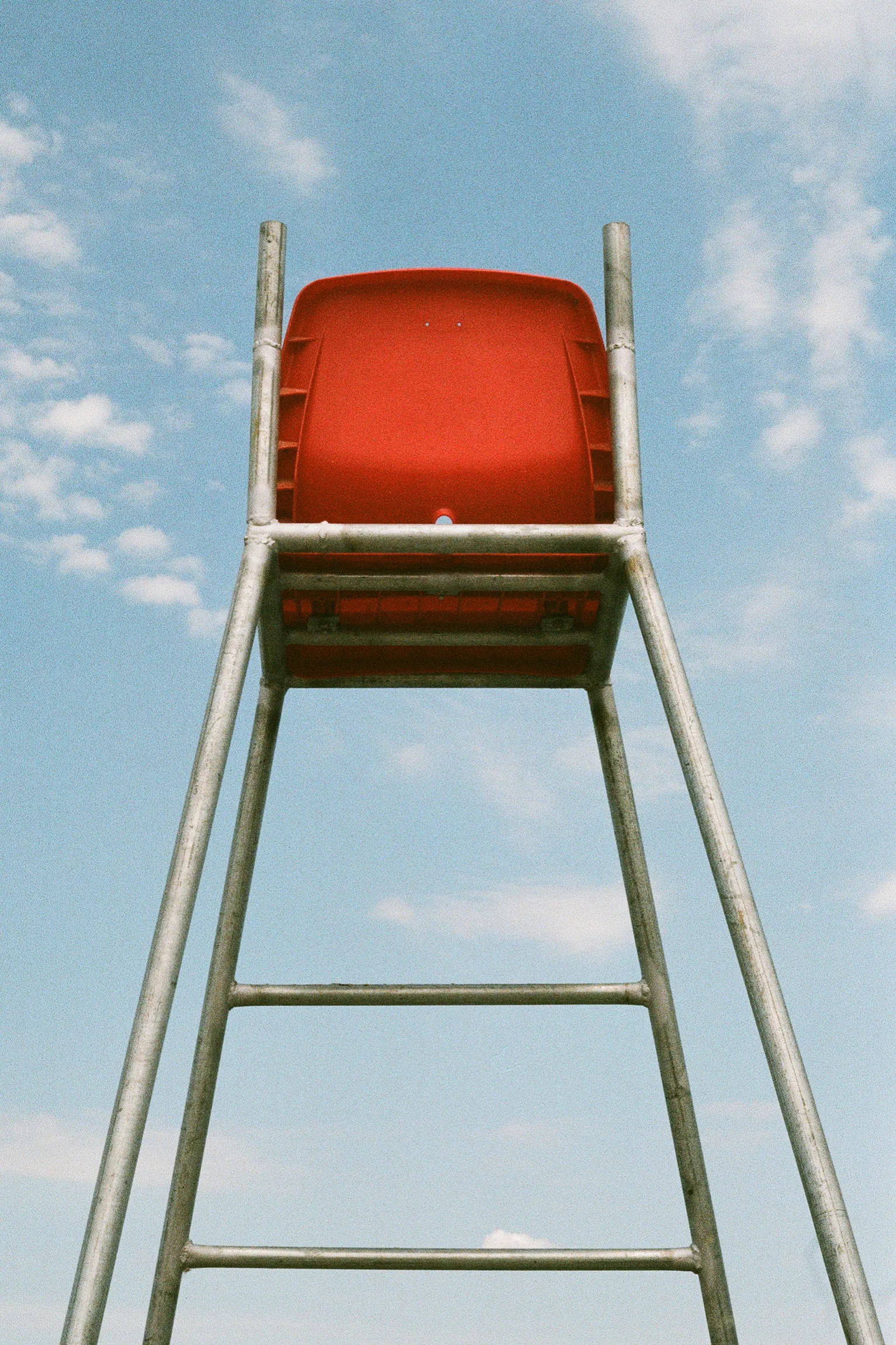 A red lifeguard chair seen from below against a pale blue sky